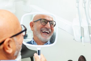 Man smiling in hand mirror looking at new smile